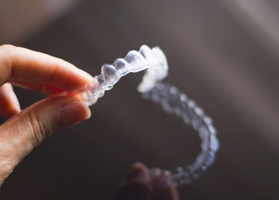 Close-up of a hand holding a clear aligner, commonly used in Invisalign treatment